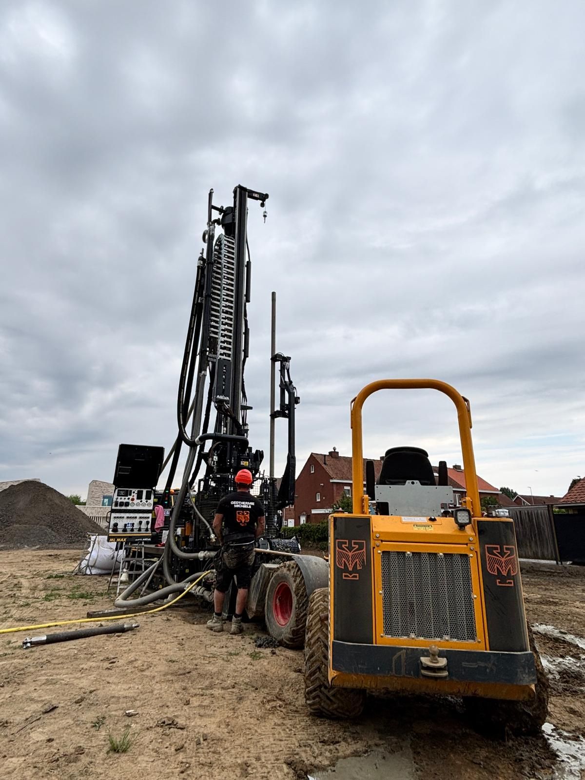 De boortoren van Geothermie Michiels aan het werk op een bouwwerf, met een ploeglid in werkkledij van het bedrijf.